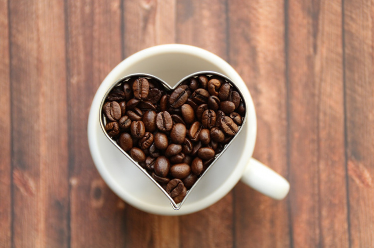 Kuvassa valkoinen kahvikuppi jossa sydämen muotoisessa muotissa kahvipapuja