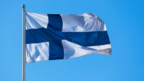 Suomen lippu lipputangossa sinistä taivasta vasten.