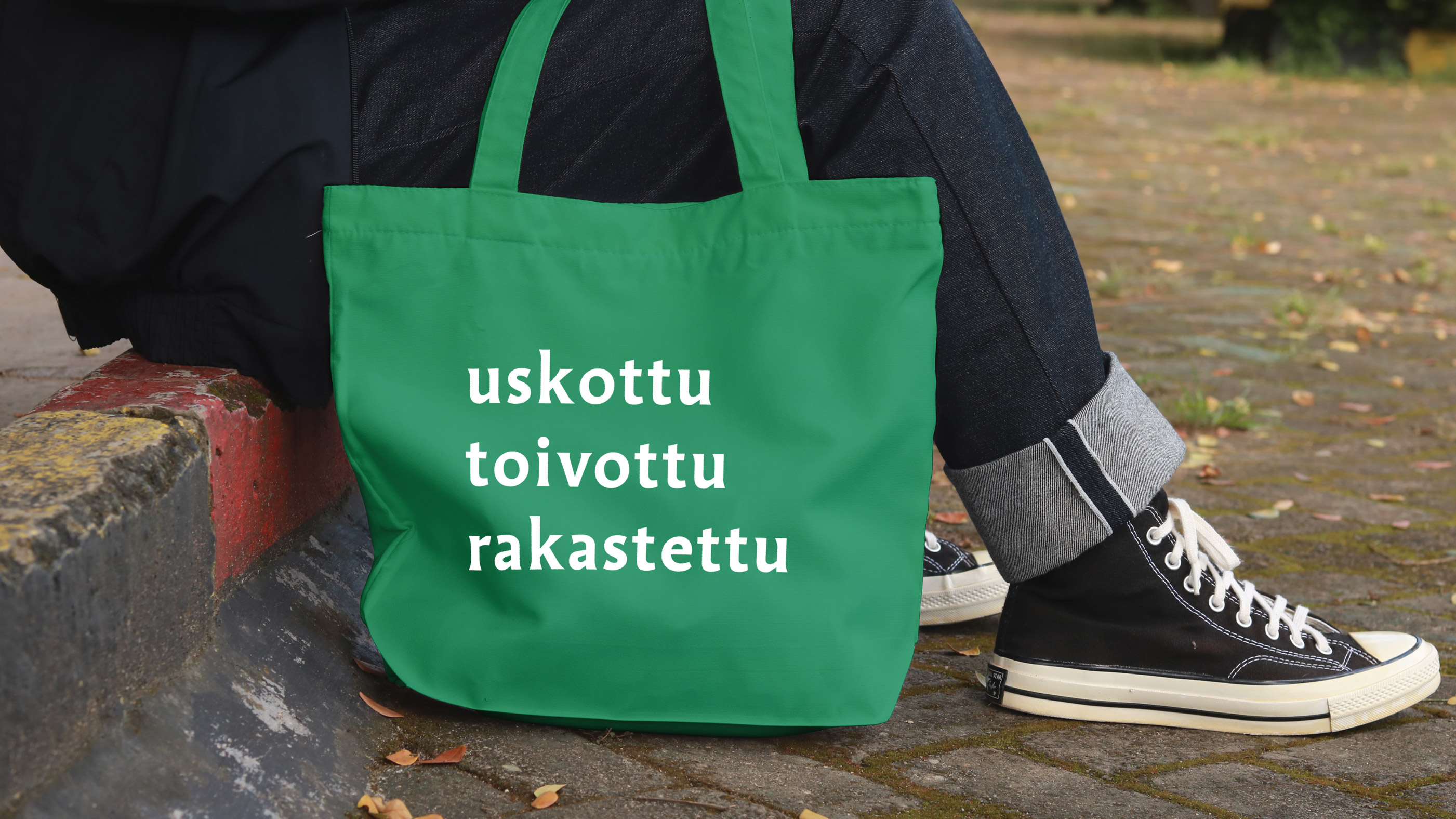 henkilö istumassa ja vihreässä kassissa teksti uskottu toivottu rakastettu.