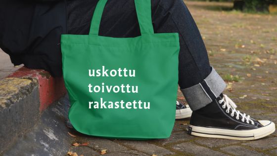 henkilöllä vihreä kassi jossa teksti uskottu toivottu rakastettu
