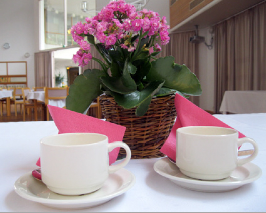 Pinkki kukkanen, pinkit servetit ja kahvikupit aseteltuna pöydälle. 