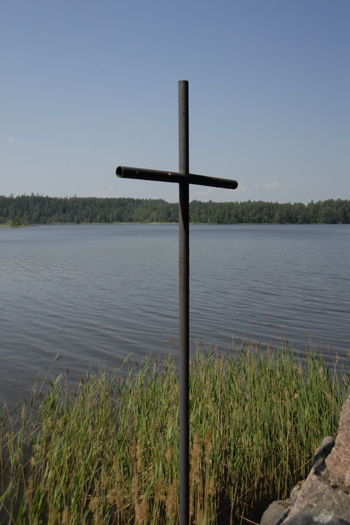 Metallinen risti leirikeskuksen järven rannalla.