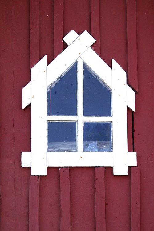 Punaisen talon seinä ja talon muodon muodostava valkokarminen ikkuna.