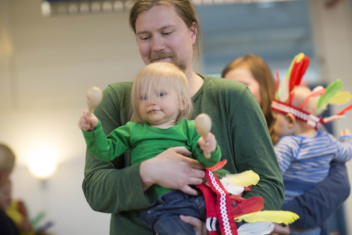 miehen sylissä lapsi, jolla on marakassit käsissä.