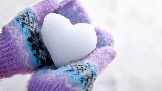 Lumesta muotoiltu sydän värikkäissä liilan värisissä hanskoissa olevien käsien varassa.
