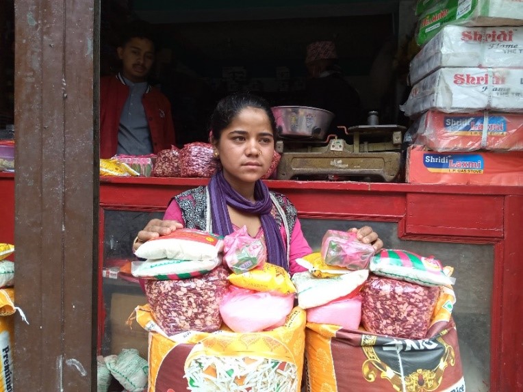 Nepalilainen tyttö, edessään erivärisiä pusseja ja takana nepalilainen ruoka-kioski.