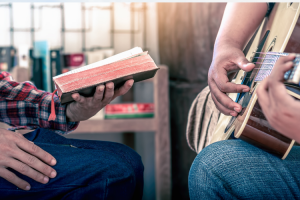 Mies pitää raamattua kädessä, toinen soittaa kitaraa.