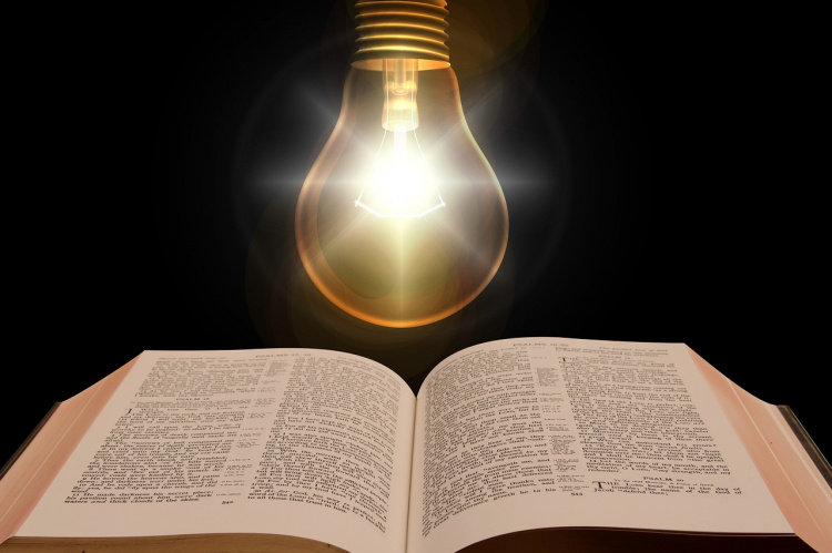 Kuvassa Raamattu jonka päällä on palava hehkulamppu