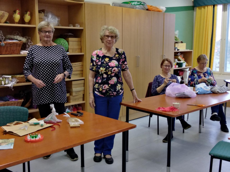 Lähetyksen käsityöryhmä Kuvassa neljä naista, pöytien takana, kaksi seisoo ja kaksi istuu ja kutoo, Pöydillä käsityötarvikkeita.