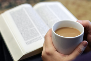 Raamattu ja kahvikuppi kädessä.