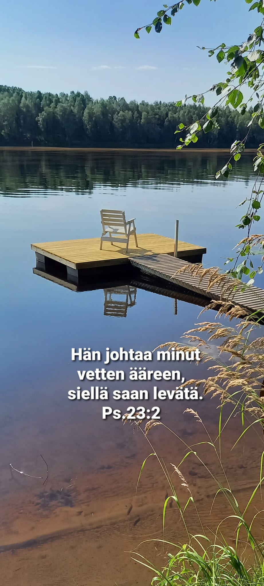 valoisa järvimaisema, jossa tuoli laiturilla ja teksti "Hän johtaa minut vetten äärelle, siellä saan levätä."