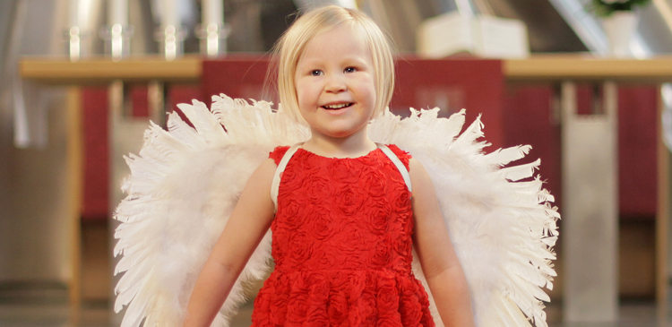 Keravan kirkon alttarilla pikkutyttö punaisessa mekossa ja enkelinsiivet selässä.